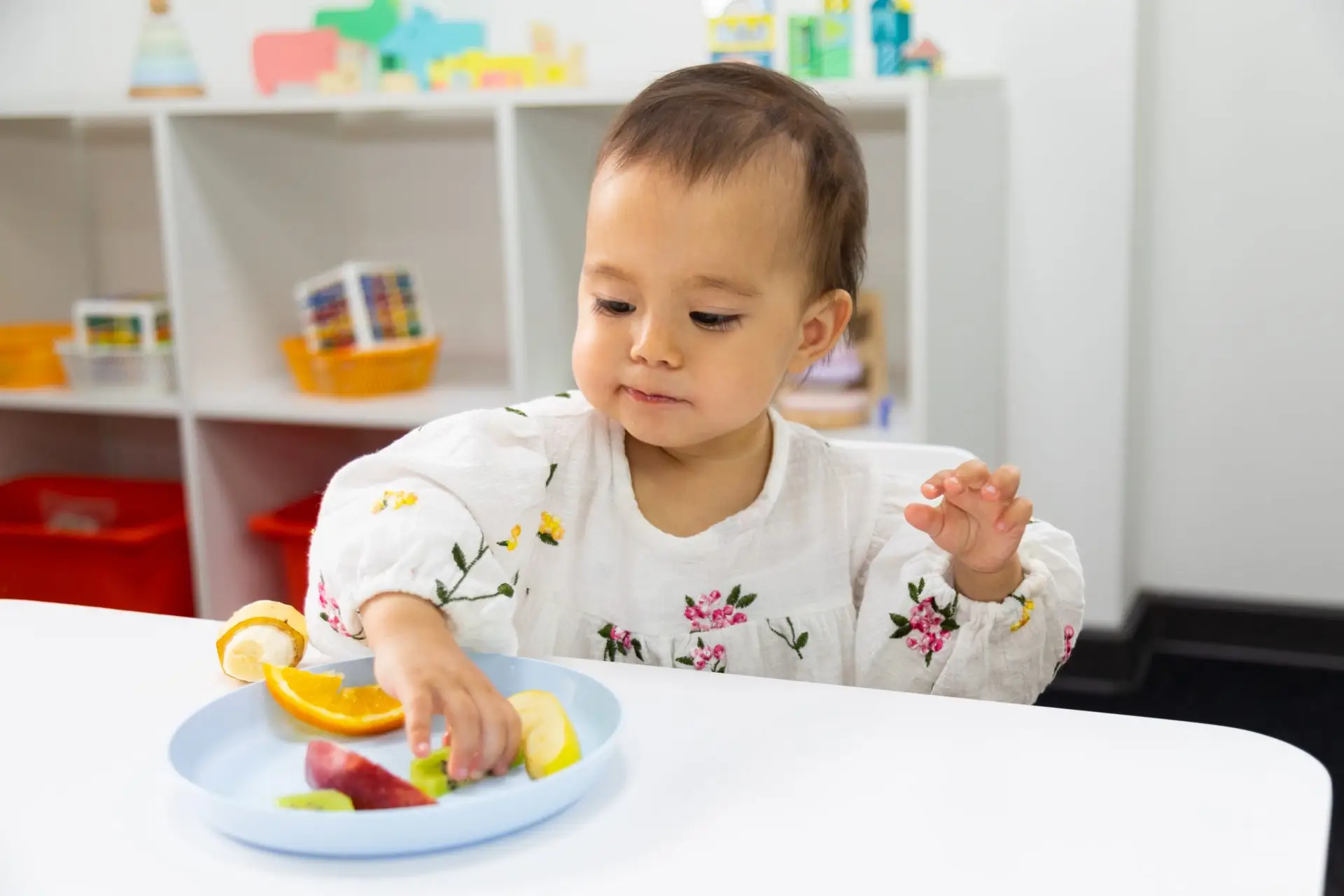Toddler eating fresh cut fruit from a plate at nursery Nursery Rhymes Broughty Ferry